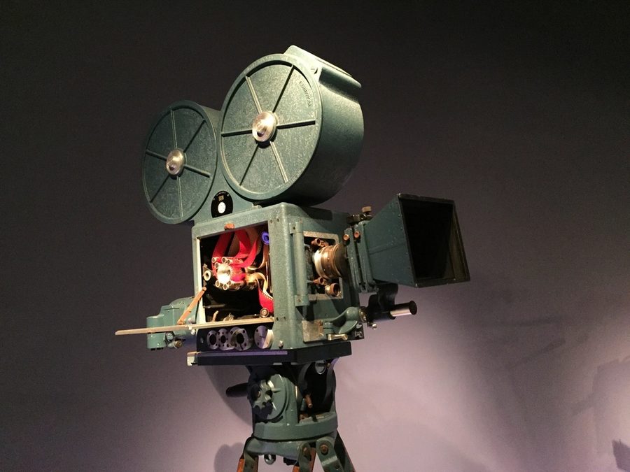 A vintage film projector on a stand against a dark ground